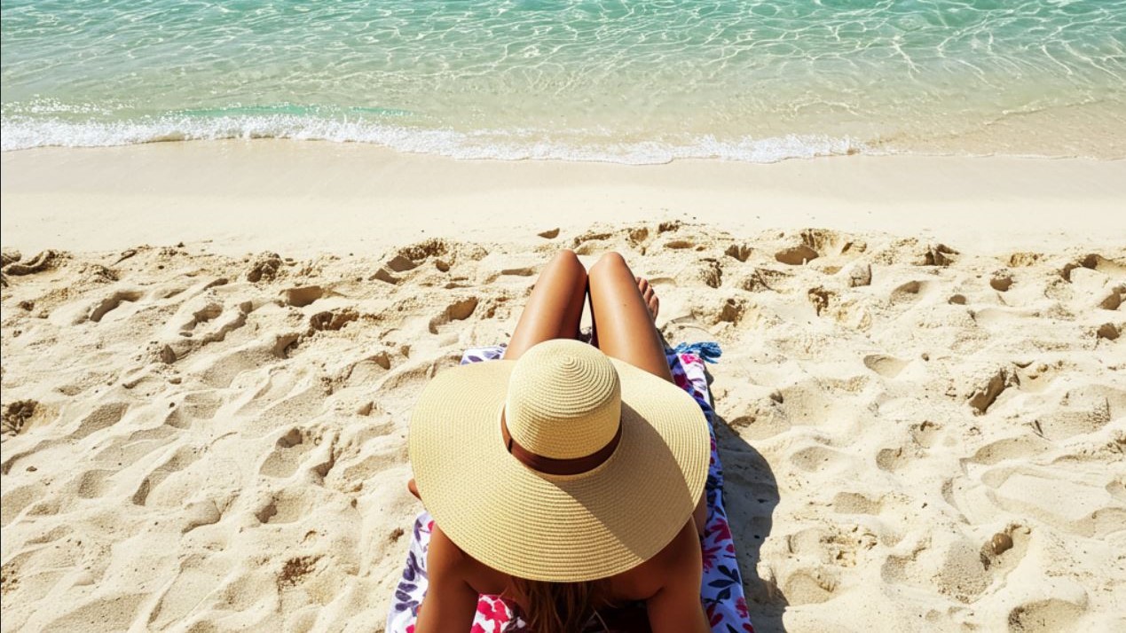 Une femme avec une pamela qui prend le soleil sur une plage Canarienne.